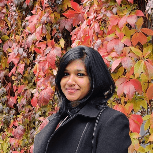 Ashden team member, Nashwa Naushad smiling in front of a wall of leaves