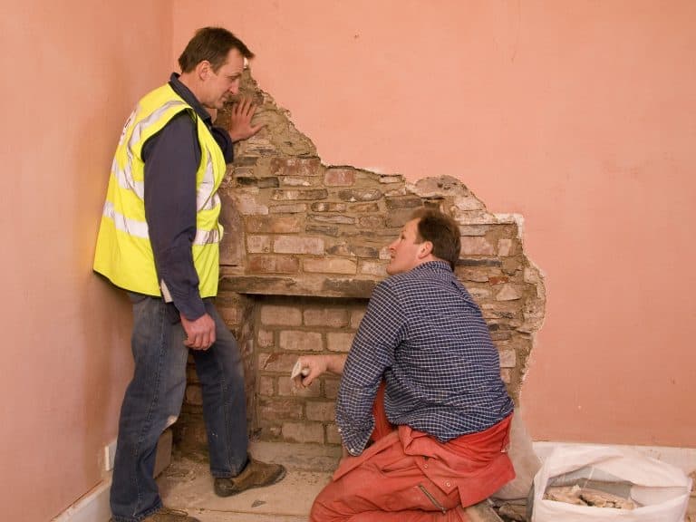 Two workmen look at exposed brickwork