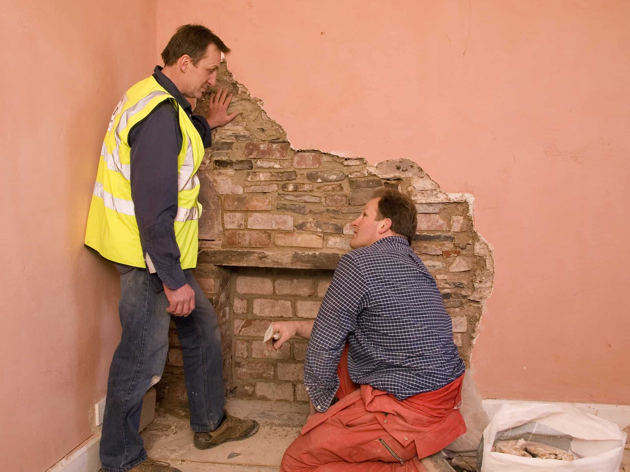 Two workmen look at exposed brickwork