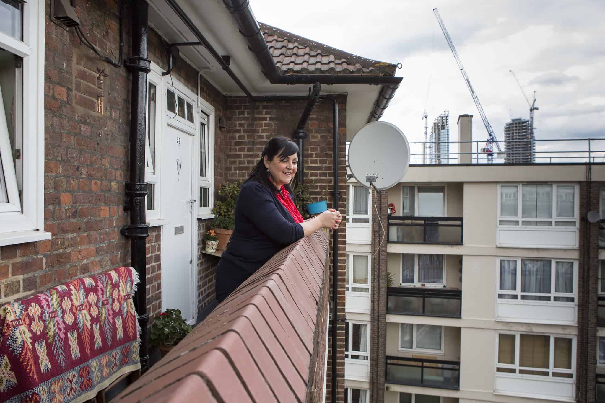 A woman standing on a balcony on a council estate looking at the camera