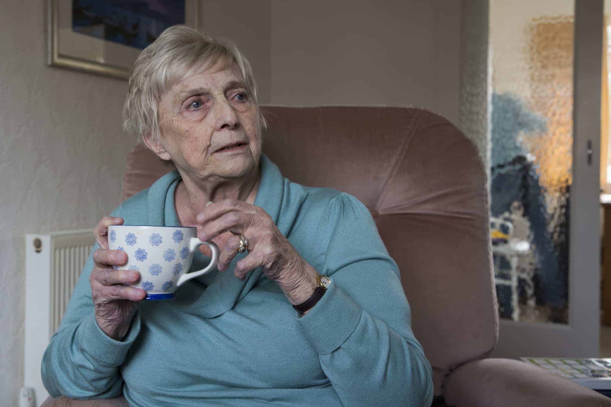An older woman with a cup of tea sitting in arm chair