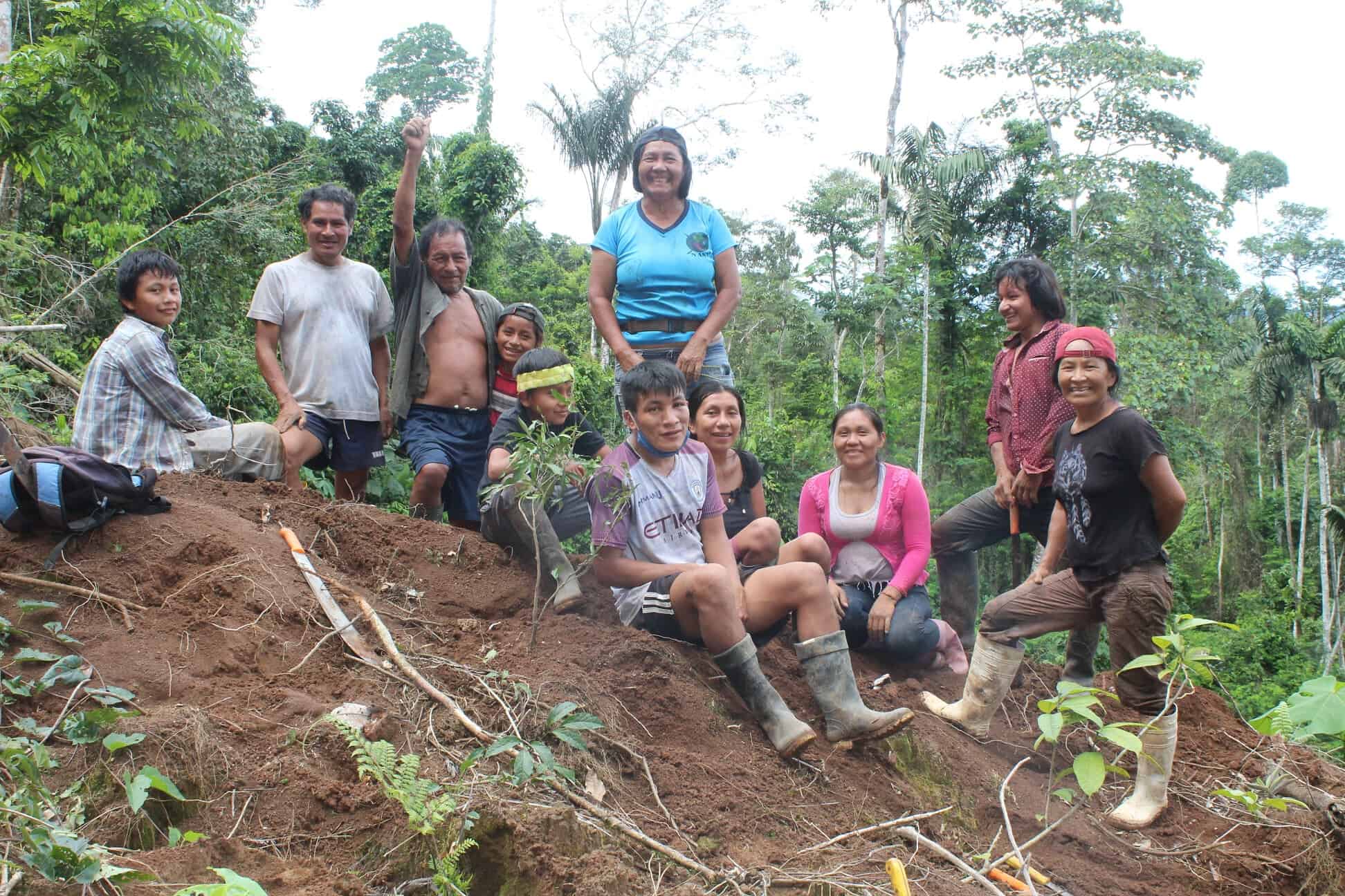 A group of Indigenous women and their families sit together on a small hill in the rainforest.