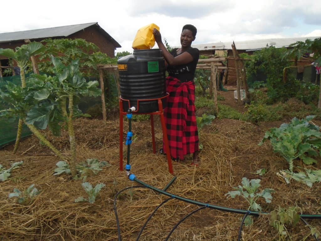 A female farmer fills her mobile drip-irrigation kit with a yellow bucket.