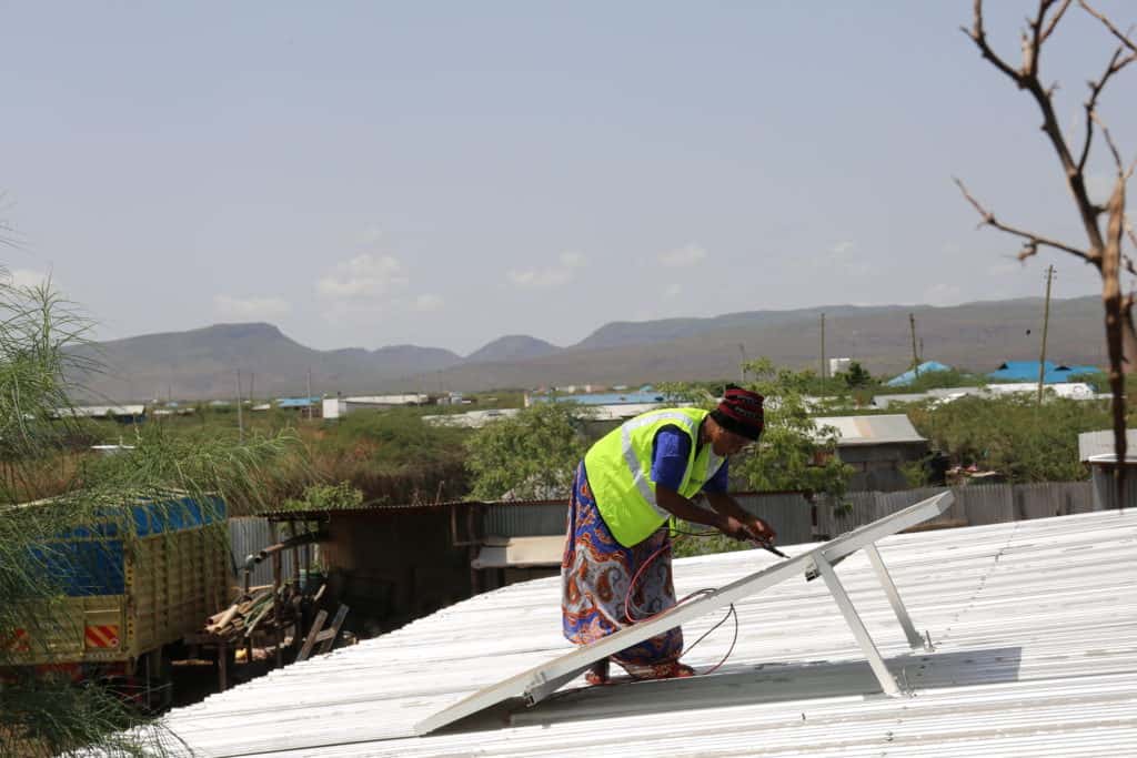 A female solar panel installer checks a solar panel on a hotel roof.