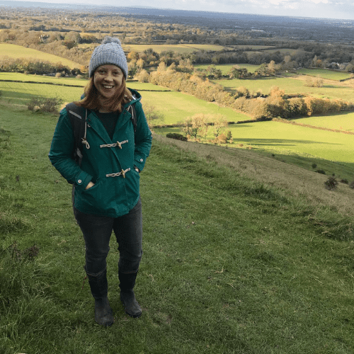 Ashden team member, Catherine True, a woman wearing a green coat on a hill with the countryside behind her