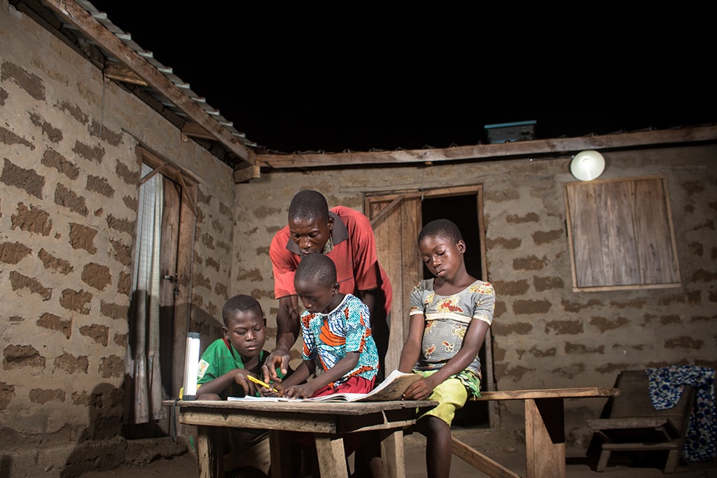Credit gov of Togo - A father helping his children with their homework at night under a solar light