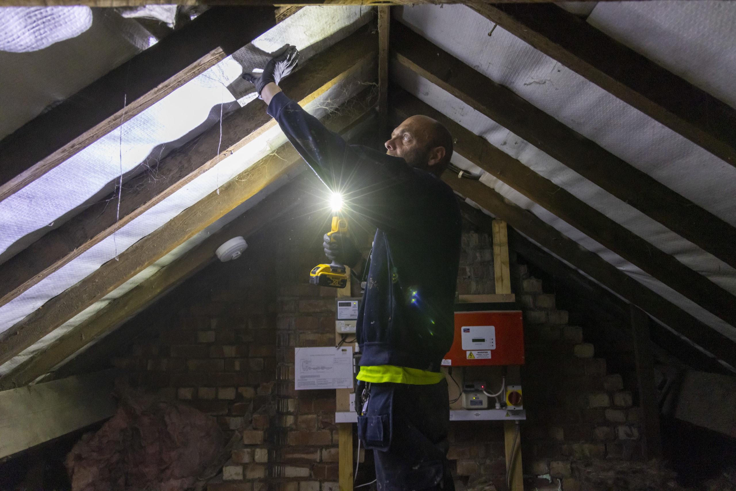Man holds a flashlight and works on insulation in a attic space