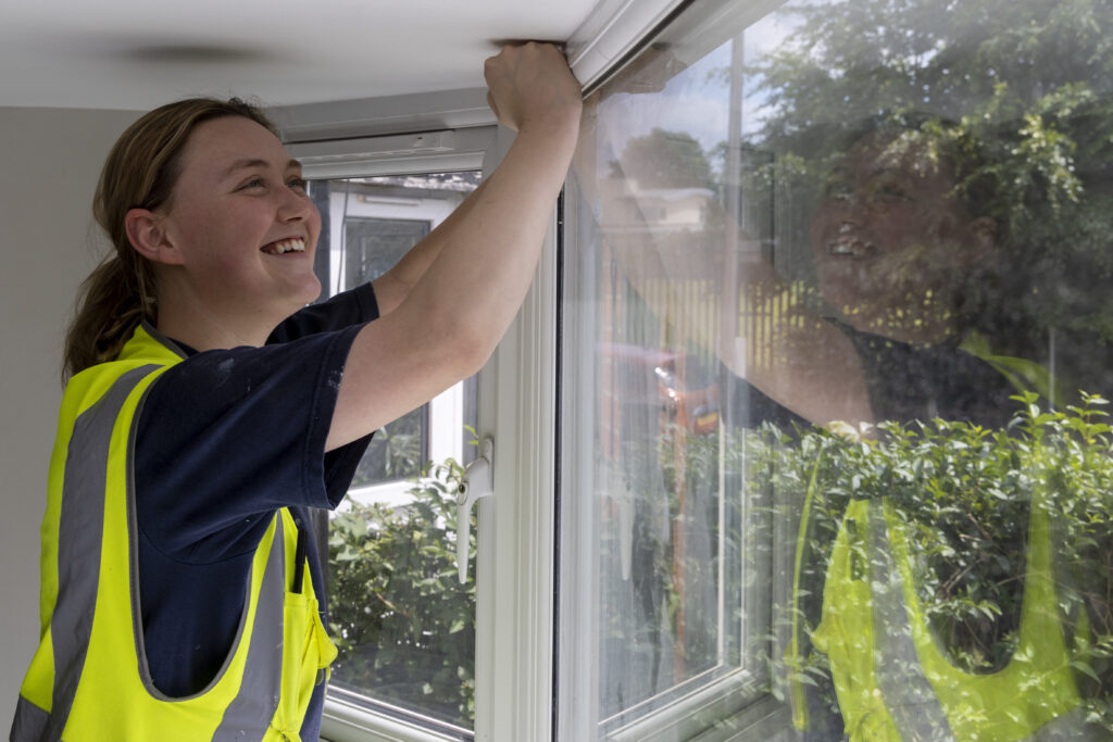 Woman in high-vis vest smiles and works on a window