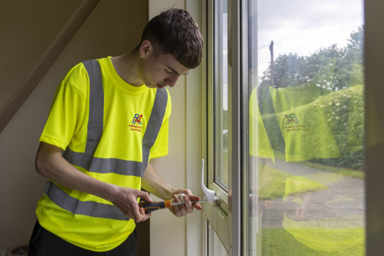 Young man in a high-vis shirt using a screwdriver to work on a window.