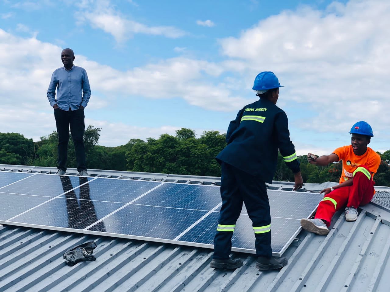 Three male trainees installing solar panels on a roof