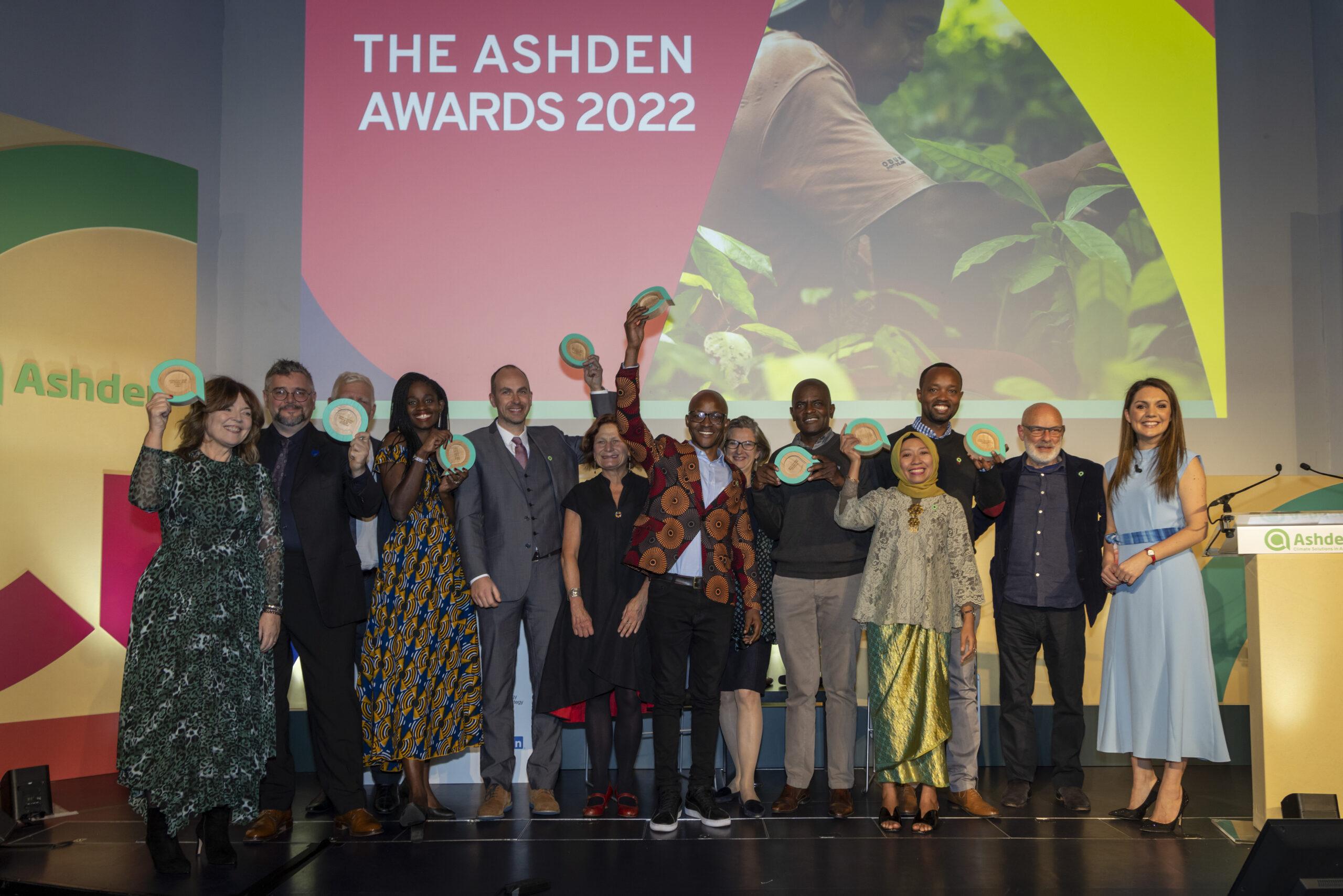 13 people pose on awards stage. Background screen reads "The Ashden Awards: 2022"