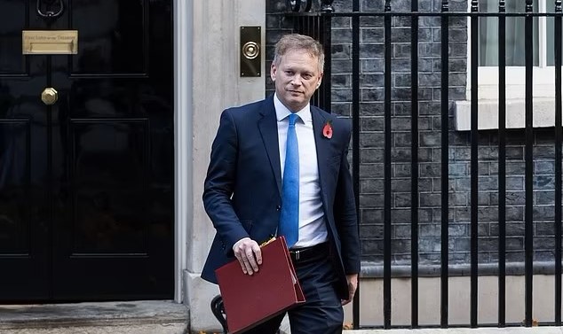 Member of Parlaiment Grant Shapps wearing a suit and walking while holding a maroon folder