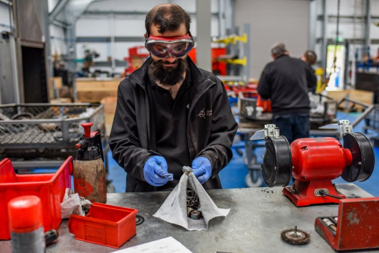 Man in protective goggles at a workshop table working with metal