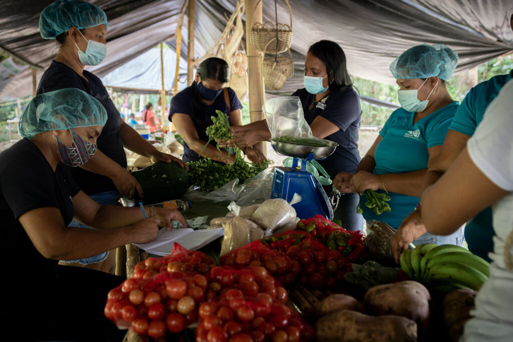 Five women in masks and hair nets working around a table of vegetables.