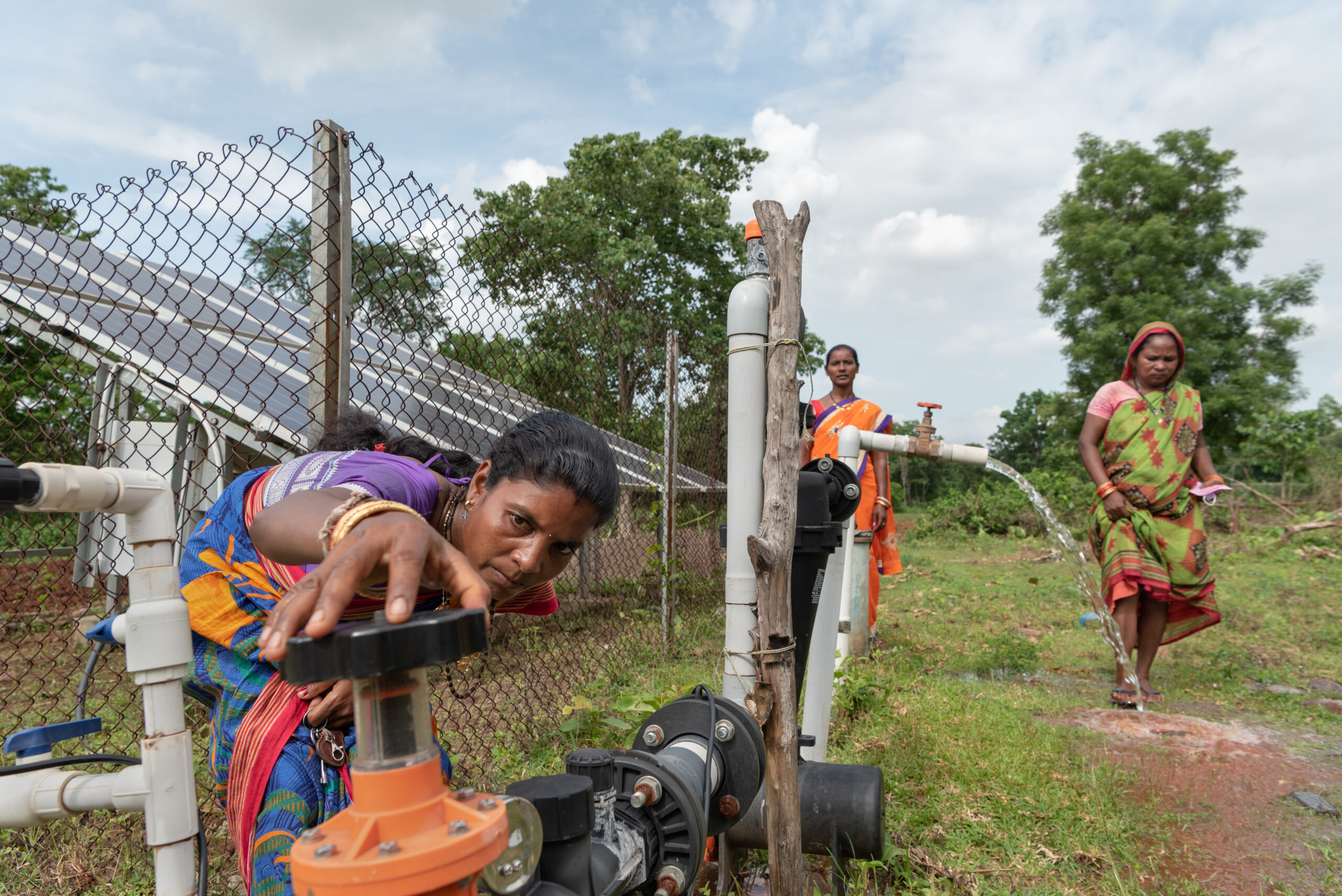 Women operating a solar water pump and two women turning on the taps to regulate water supply