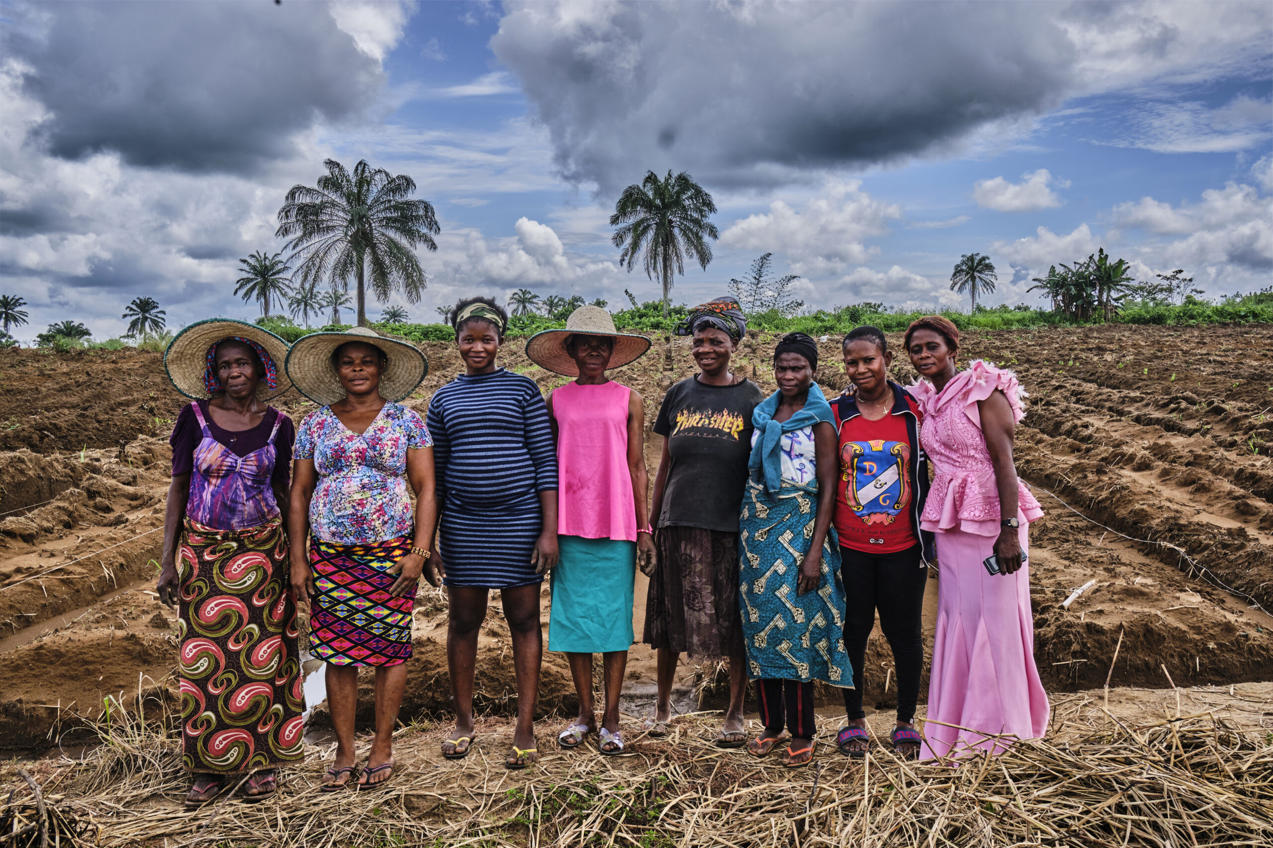 Eight women stand in front of a dirt field prepared for irrigation.
