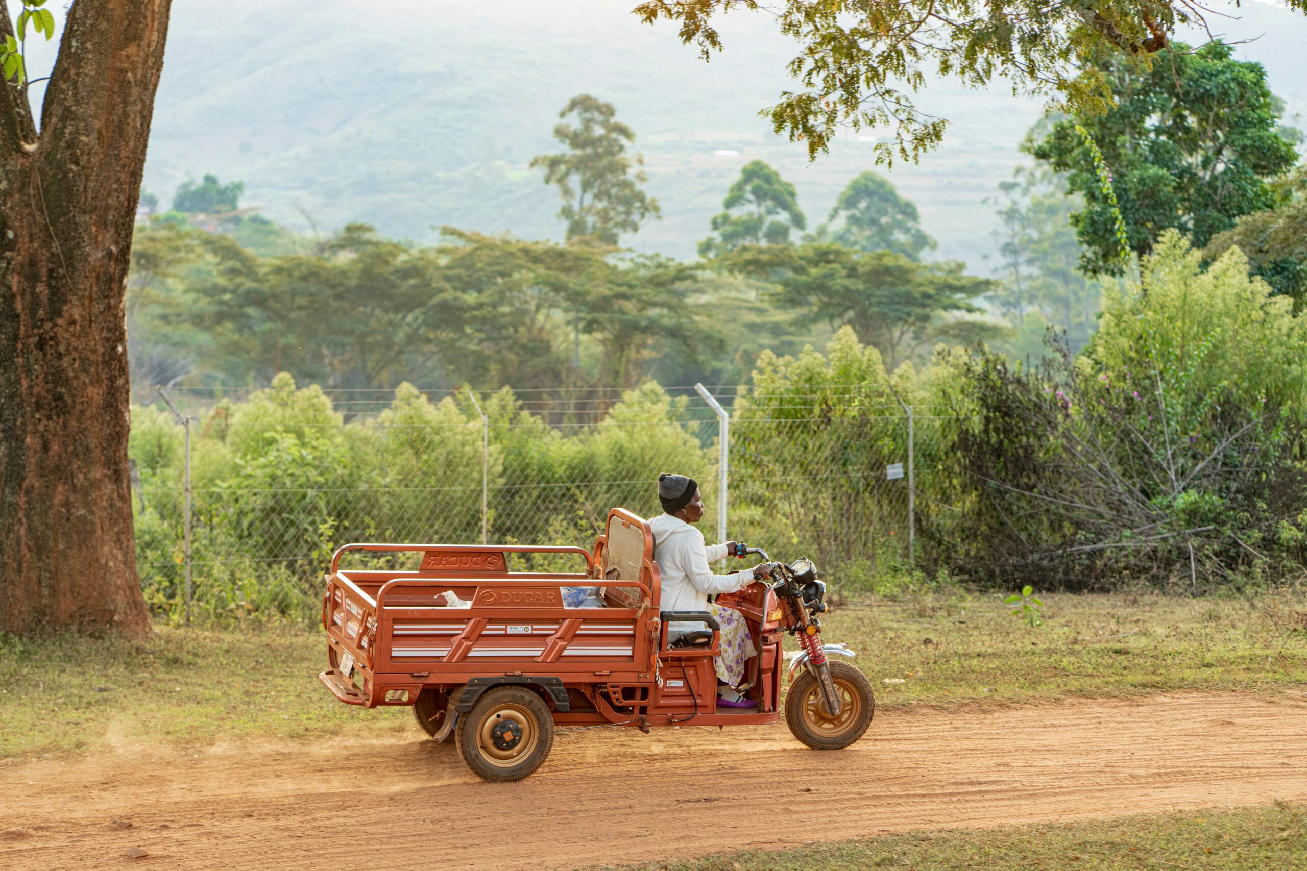 Woman riding an electric tricycle along a a rural dirt road.