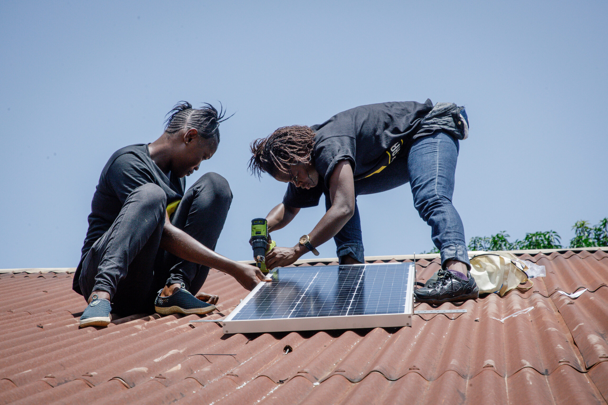 Two women installing a solar panel on top of a roof.