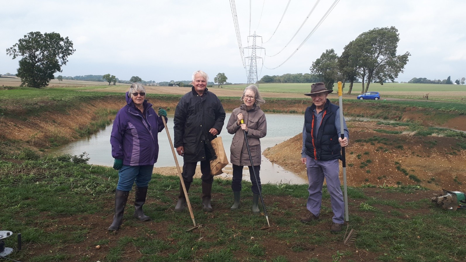 4 people standing with gardening tools in front of a pond