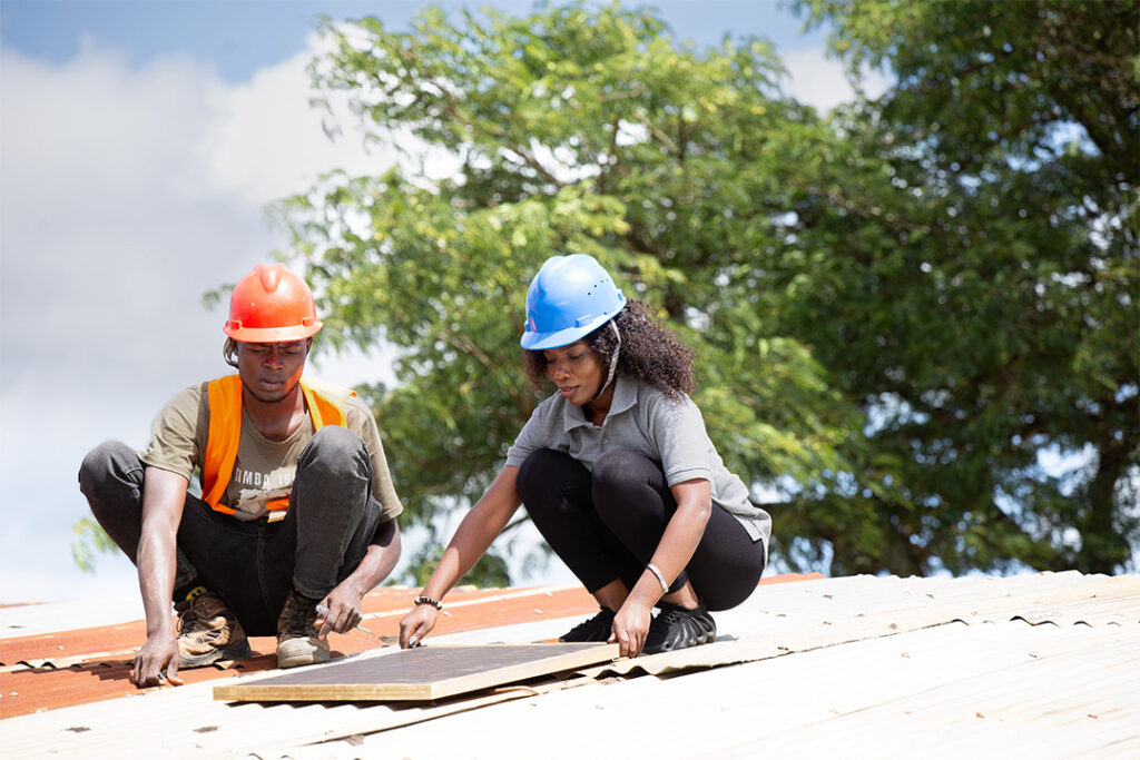 A male and female installing solar panels on a roof