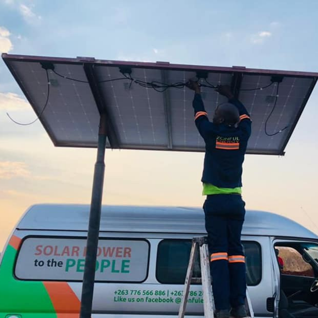 A man works on solar panel above him. A silver van behind him reads "solar power to the people"